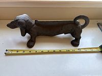 Side profile image of cast iron dachshund dog boot scraper showing curled tail and length with tape measure.