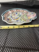 Top view of hand-painted ceramic dish featuring bird and floral designs with measuring tape showing length of approximately 8 inches.