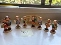Full view of the collection of seven small Hummel porcelain children figurines displayed on a windowsill, showing all figures in a row with a note labeled #50.