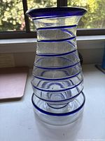 Full view of clear hand blown glass hurricane lantern with cobalt blue spiral trim, showing shape and color details.