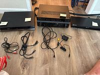 Three home theater electronic devices: Pioneer AV receiver in center, Toshiba HD DVD player on left, Sony 3D Blu-Ray player on right, with cables on floor in front.