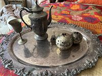 Large silver plated on copper serving tray with ornate grape and leaf border, holding silver plated coffee pot, goblet, two star votif candle holders, and small heart basket