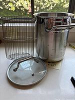 Full set of stainless steel pot, wire basket insert, and glass lid arranged on kitchen counter with natural light.