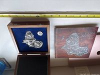 Wooden box open showing pewter puzzle of Africa with Big Five animal figures raised in relief, blue felt lining, wooden case, and puzzle box cover with depiction of the puzzle