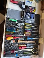 Top down view of the tools spread out on a black foam surface showing screwdriver set, pliers, hammer, files, and socket set