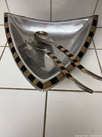 Triangular vintage cast aluminum art bowl with amber and onyx accented rim, accompanied by matching serving spoon and fork with amber and onyx handles inside the bowl.