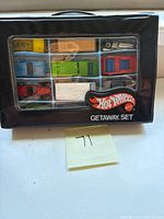 Front view of closed black Hot Wheels Getaway Set carrying case with 12 cars visible through clear window.