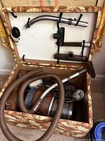 Full view of the vacuum with hose and metal extension tubes stored in a patterned fabric case with accessories attached to the lid.