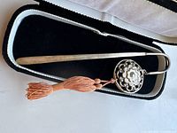 Full view of vintage silver metal bookmark placed inside black fabric-lined case showing floral decorative piece and copper tassels.