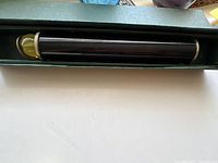 Full length photo showing black lacquered kaleidoscope with brass edging inside green original box.