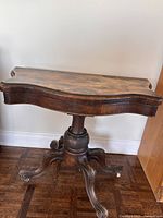 Full view of antique marbled wood side table against wall, displaying curved top and pedestal base.