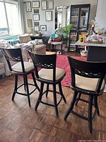 Three dark brown wooden bar stools with cream-colored cushions displayed from the back showing the lattice back design and bar stool height.
