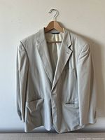 Front view of the light beige Brooks Brothers 346 stretch suit jacket on hanger showing the notch lapels, pockets, and buttoned cuffs.