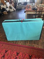 Folded thick padded light blue mat standing upright, showing its compact shape and red ties securing the fold.