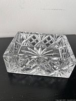Clear rectangular Galway crystal decorative box with intricate cut starburst pattern in the base, resting on black surface against white wall.