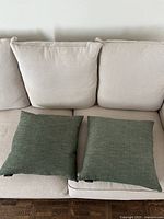 Two green 18x18 inch couch cushions placed on a beige couch, showing front of cushions.