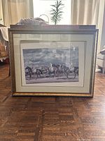 Front view of the large ornate gold picture frame with print inside displaying horses and riders.