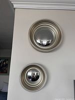 Two silver framed round convex mirrors of different sizes hanging on a white wall, showing the overall look and relative scale.