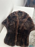 Dark brown real fur wrap shawl folded on white surface, showing soft dense fur texture.