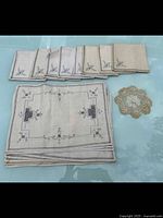 Full set of 8 embroidered napkins, 8 placemats stacked, and 1 crochet lace doily on glass table.