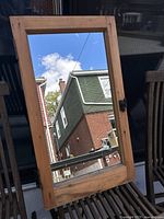 Front view of tall rectangular antique window mirror showing reflective glass and natural wood frame with metal latch.