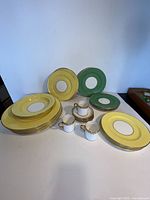 Set of assorted Aynsley and Royal Chelsea bone china plates in pale yellow and teal green colors arranged with cups and saucers.