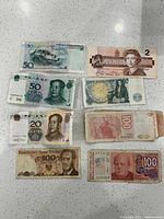 Photo showing nine assorted foreign currency bills including Canadian, Chinese, British, Polish, and Argentine notes laid out on a white surface.