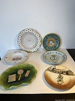 Full view of six assorted vintage ceramic plates arranged on a white surface showing different styles and designs, green textured Bretby plate at front.