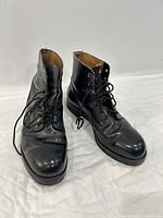 Pair of black leather lace-up boots standing on white surface, showing round toe and front view.