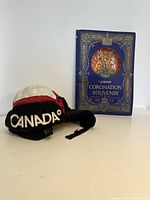 Photo of the Canada Olympic hat and the 1937 Coronation Souvenir book side by side on a plain surface