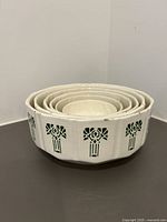 Stacked nesting set of six ceramic bowls, white base with green floral design, showing size gradation and minor wear.