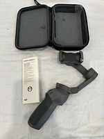 DJI Osmo Mobile 3 gimbal with carrying case and manual laid out on white surface.