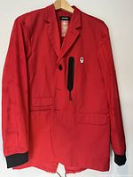 Front view of red blazer-style Olympic jacket by Dsquared2 with two front flap pockets and a vertical zipper pocket near chest, featuring the Canadian Olympic leaf patch.