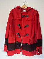 Front view of red wool duffle coat with black stripe, hood, and leather toggle closures