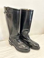 Pair of tall black leather riding boots standing upright, showing front and side views with adjustable silver buckles and harness straps.