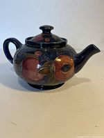 Side view of Moorcroft ceramic teapot showing fruit pattern decoration and lid.