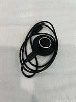 Top view of black Oura Ring charging cable coiled, showing the magnetic charging pad with connection points and cable plug.