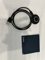 Black circular USB charger with cable and Oura manual booklet on white background