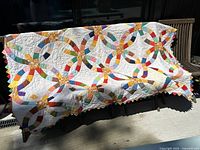 Full view of multicolor double wedding ring quilt draped over bench in sunlight