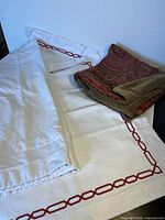 Photo of pillow shams laid out on bed showing two white shams with red chain-link embroidery and one paisley chenille-backed sham