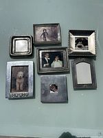 Front view of 7 assorted pewter photo frames with photos mostly black and white, including a dog image and a 'BOW WOW' frame.