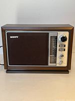 Front view of Sony radio showing wood-grain casing, speaker grille, silver control panel with tuning scale and Sony logo
