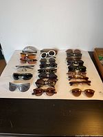 Photo showing eighteen pairs of assorted sunglasses displayed on a white surface, various colors and styles including sport, oversized, and round frames