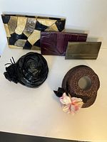 Four items displayed together: one patchwork leather clutch with a chain, two hats (one brown with floral accent, one black glossy rolled style), and an additional burgundy leather clutch or large wallet.