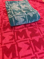 Folded teal towel placed on top of the red towel, showing geometric pattern.