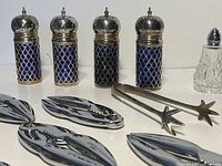 Blue latticed salt and pepper shakers with silver tops, small clear glass shaker, silver sugar tongs, and chrome lobster nutcrackers arranged closely