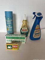 Front view of five cleaning and scent care items arranged on white background including Hagerty spray polish, Windex cleaner, Fantastik cleaner, Wet-naps box and Swan Vesta matches.