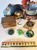 Five vintage paper masks arranged side by side behind other items, showing the detailed faces and wood box in front