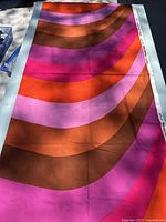 Full view of the large rectangular fabric showing the abstract colorful stripes pattern in shades of orange, pink, brown and purple