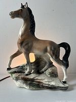 Front view of glazed prancing horse ceramic lamp on rocky base showing detailed horse form and glossy finish.